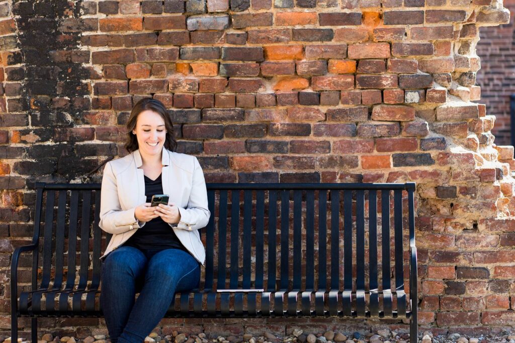 Realtor sitting on a bench outside sending emails on her phone